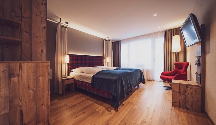 Double room with balcony, classic Swiss stone pine furnishings, lounge chair, chest of drawers and wooden floor | © Davos Klosters Mountains 