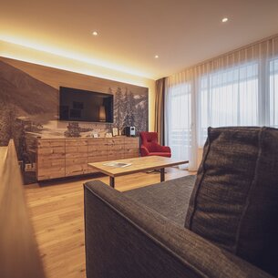 Large room with wooden floor, sofa, wooden chest of drawers and TV | © Davos Klosters Mountains 