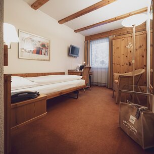 Simple single room furnished with Swiss stone pine furniture, chair and floor lamp  | © Davos Klosters Mountains 